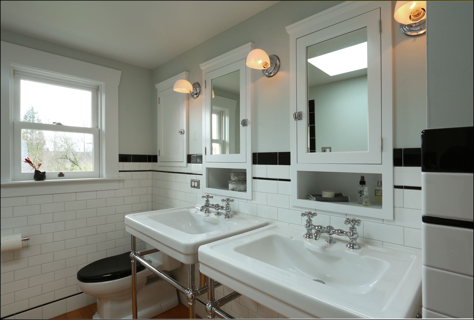 Bright bathroom with dual sinks, large mirrors, white tile, and a window.