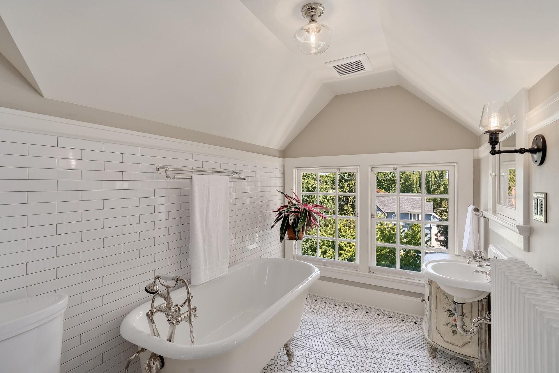 Occupying the dormer of a historic Irvington home, this charming bathroom was remodeled with the original period style in mind, including a clawfoot tub, wall-mounted sink, and a classic white hex-tile floor. 