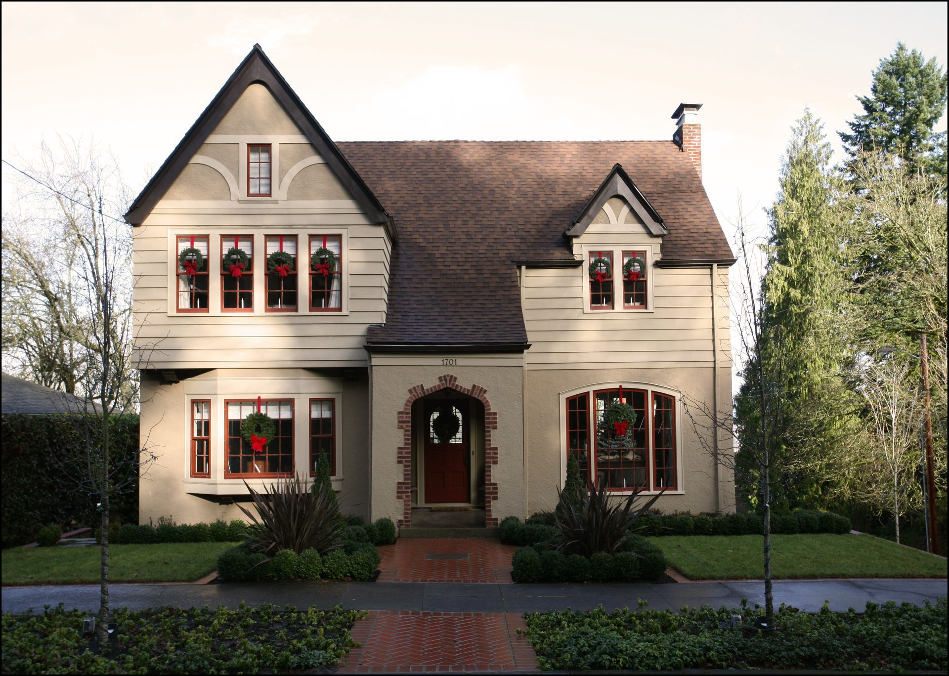 Two-story cream house with dark roof, arched front door, and manicured lawn in a suburban setting