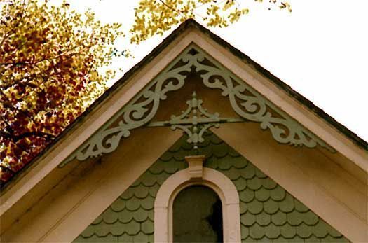 Ornate green house gable with decorative trim and a small arched window beneath autumn leaves
