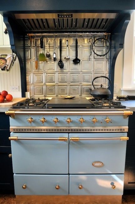 Blue vintage stove with brass knobs and hanging utensils beneath a black range hood in a kitchen