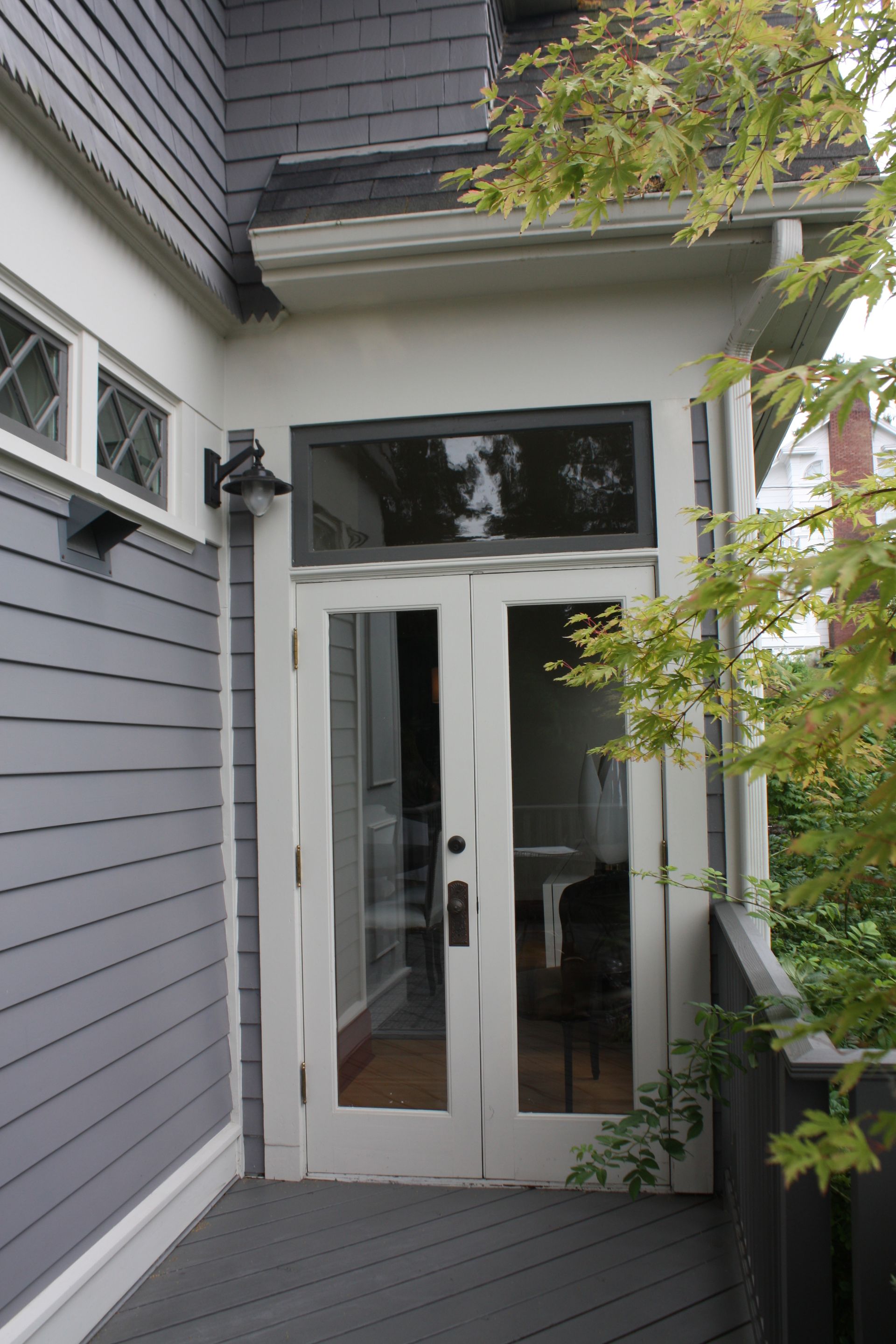 White double glass doors at the entrance of a gray house, framed by trees and siding.