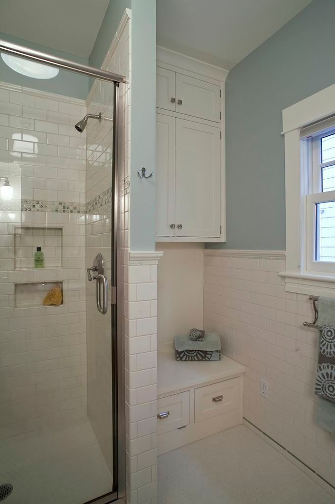 Bathroom with glass shower, white tile, built-in cabinet, and window with shutters.
