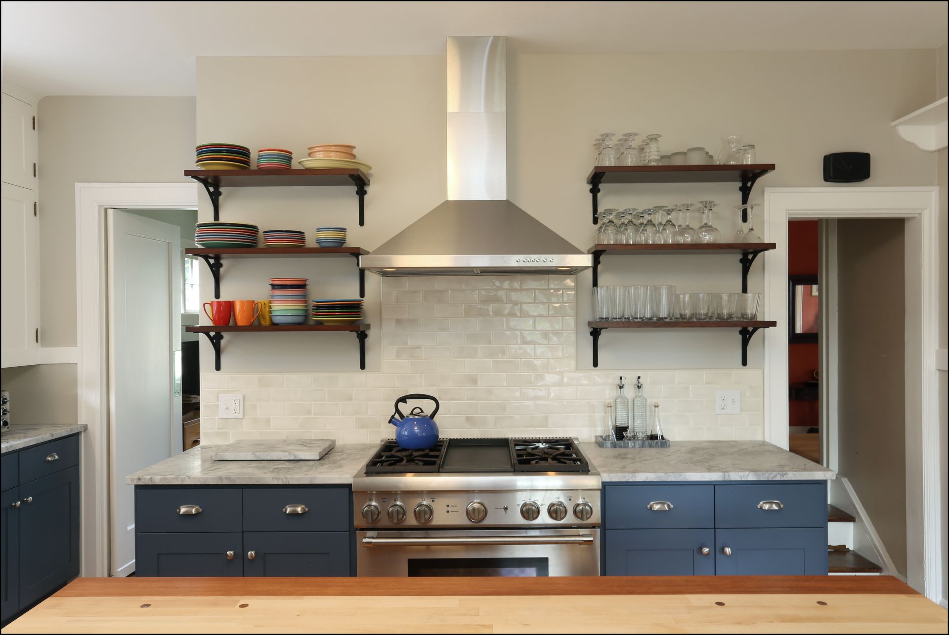 Modern kitchen with blue cabinets, white tile backsplash, stainless range, and open shelves