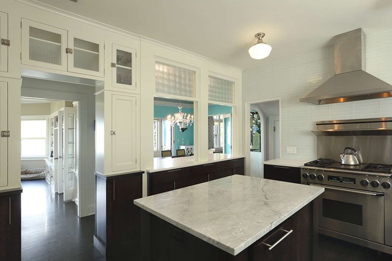 Modern kitchen with marble island, stainless steel stove, white cabinetry, and dark wood floors