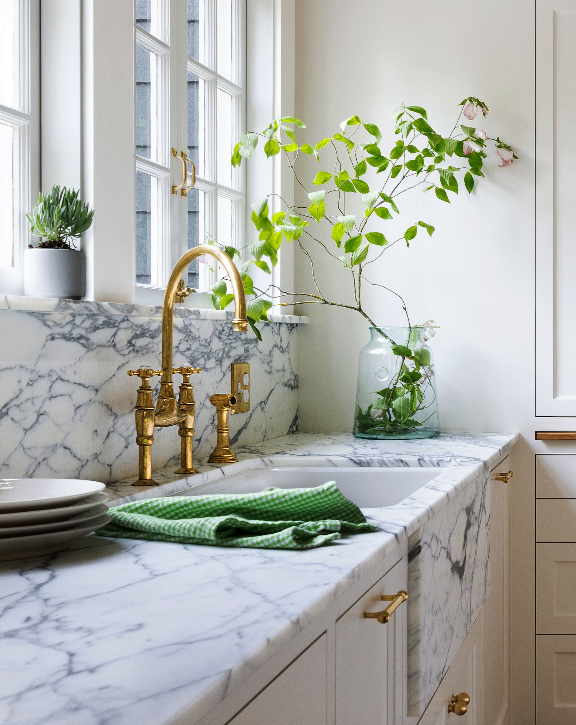 Under a generous pair of windows, the   Arabescato marble counter and backsplash and the unlacquered brass faucet look beautiful in the light.