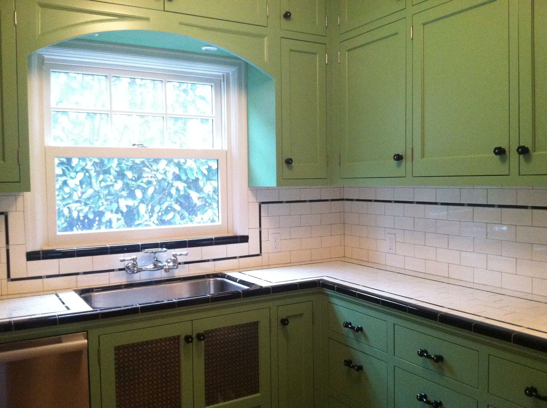 Green kitchen with black countertops, white tile backsplash, and a window above the sink.