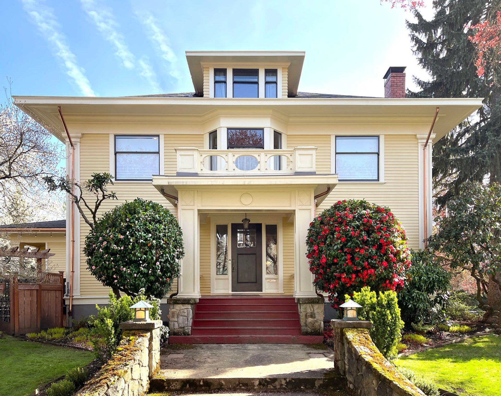 Pale yellow 1911 Craftsman Foursquare with distinctive rail around porch balcony roof.