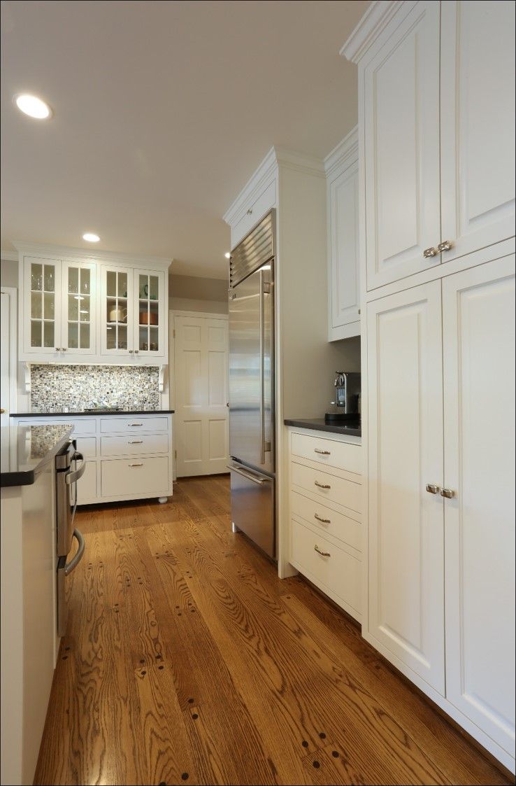 Bright white kitchen with wood floors, built-in cabinets, and stainless steel refrigerator.