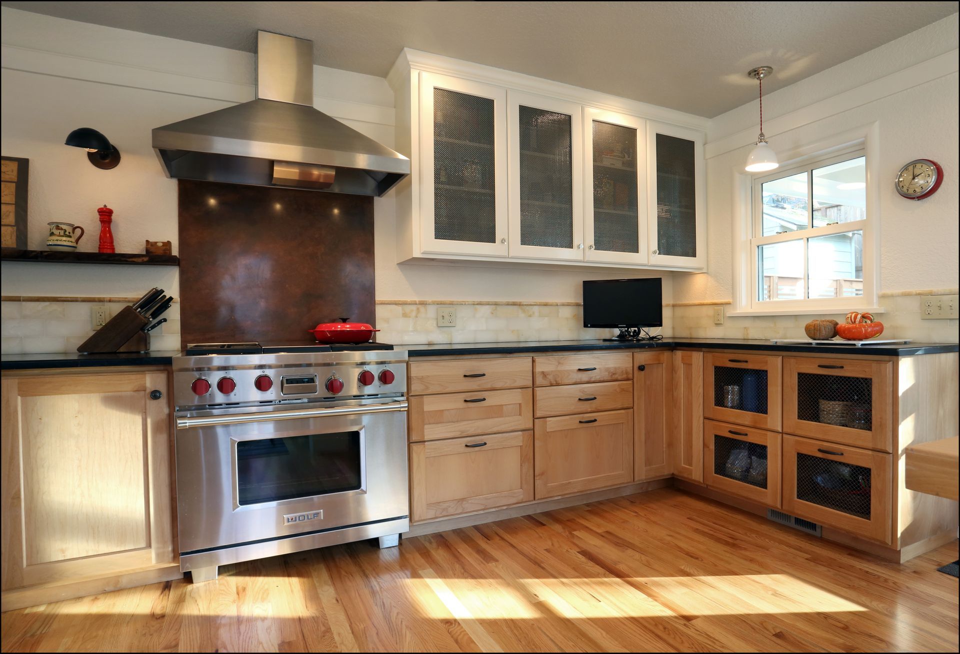 Modern kitchen with stainless steel stove, wood cabinets, white upper cabinets, and sunlit hardwood floor