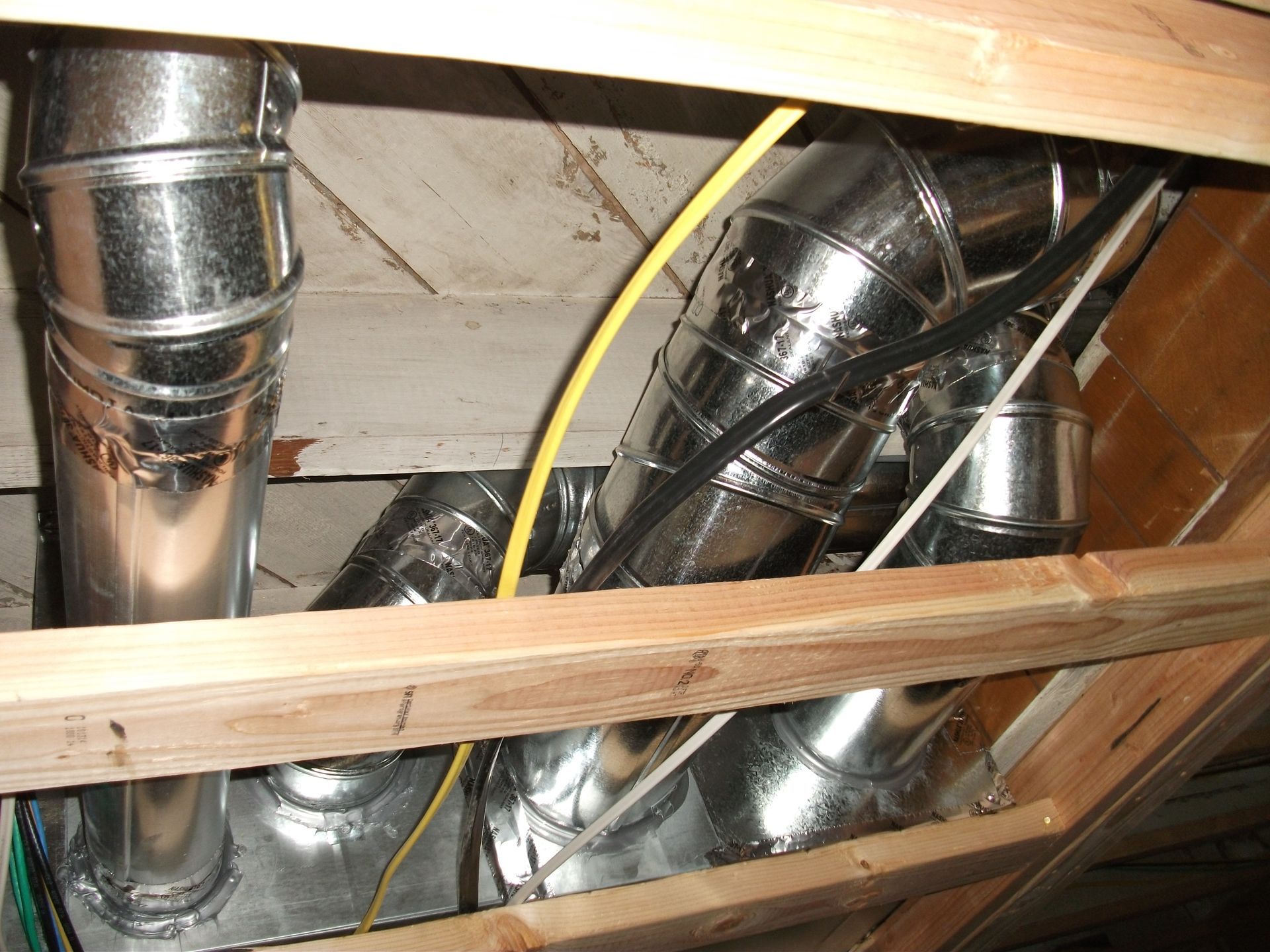 Exposed shiny metal HVAC ducts and a yellow cable running through attic rafters