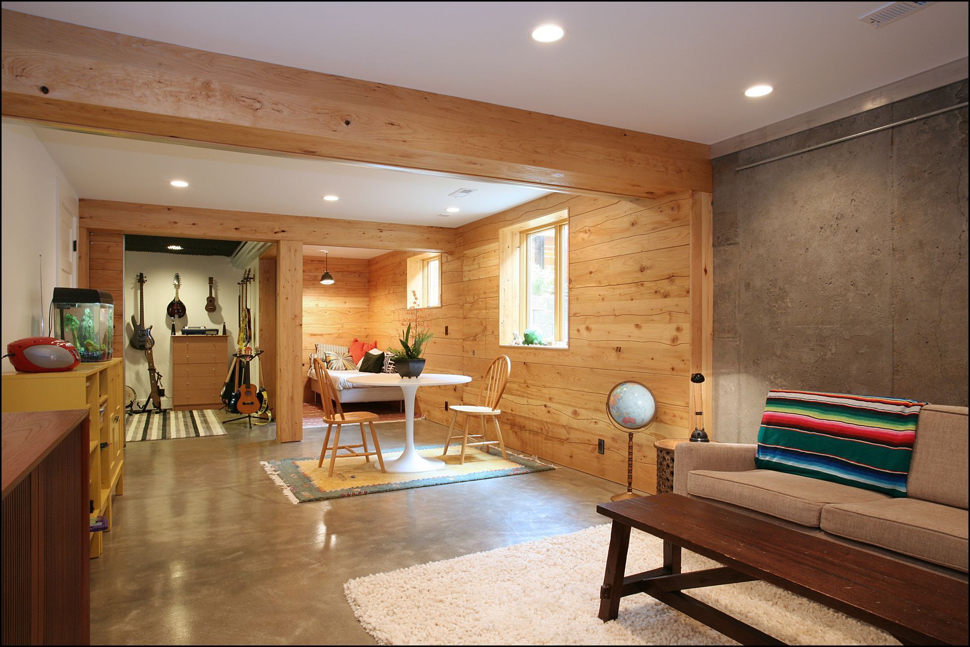 Modern open-plan living room with wood walls, a sofa, dining table, and large window