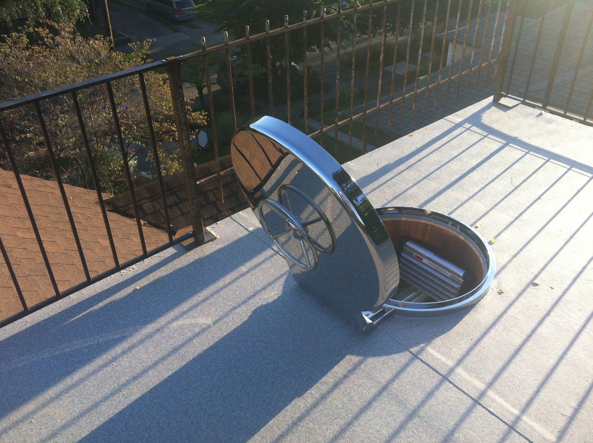 Round skylight window open on a rooftop deck beside a black railing.
