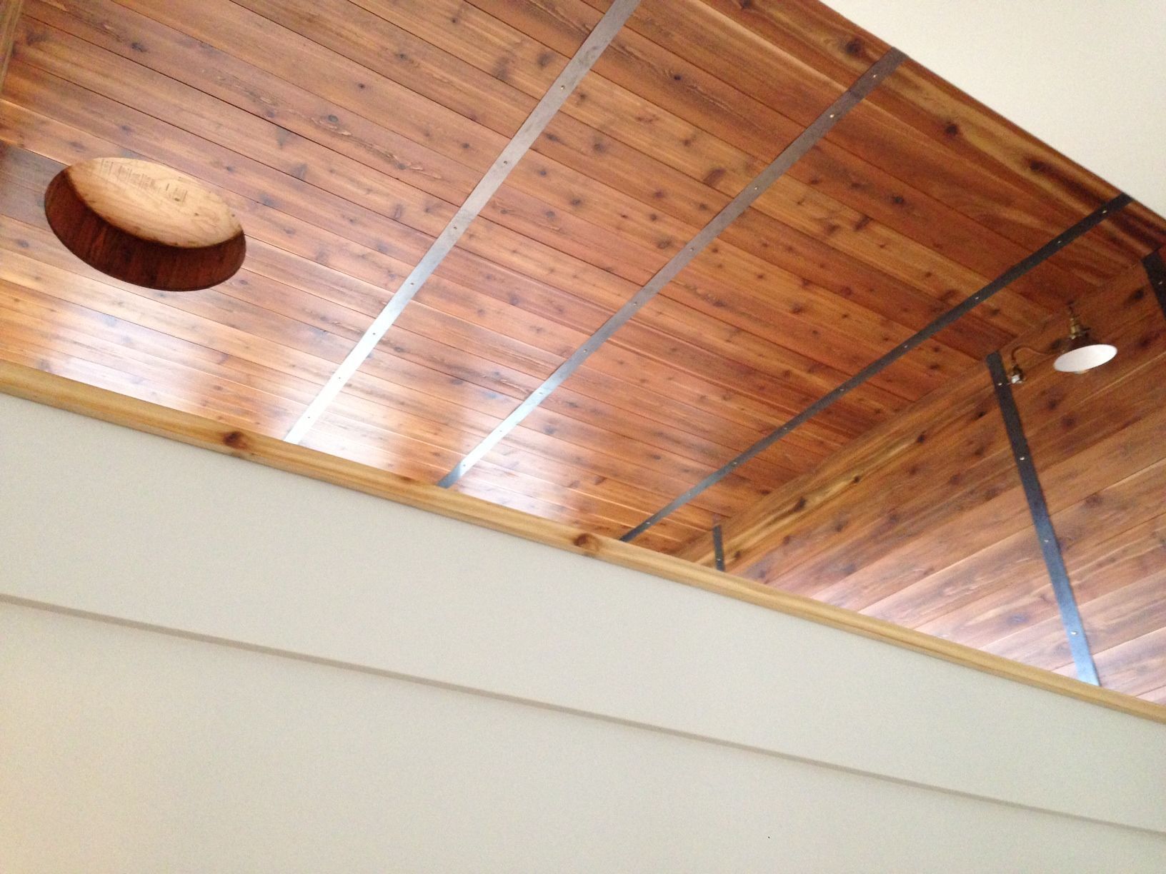 Wood-paneled ceiling with metal beams and a small round light fixture above a cream wall.