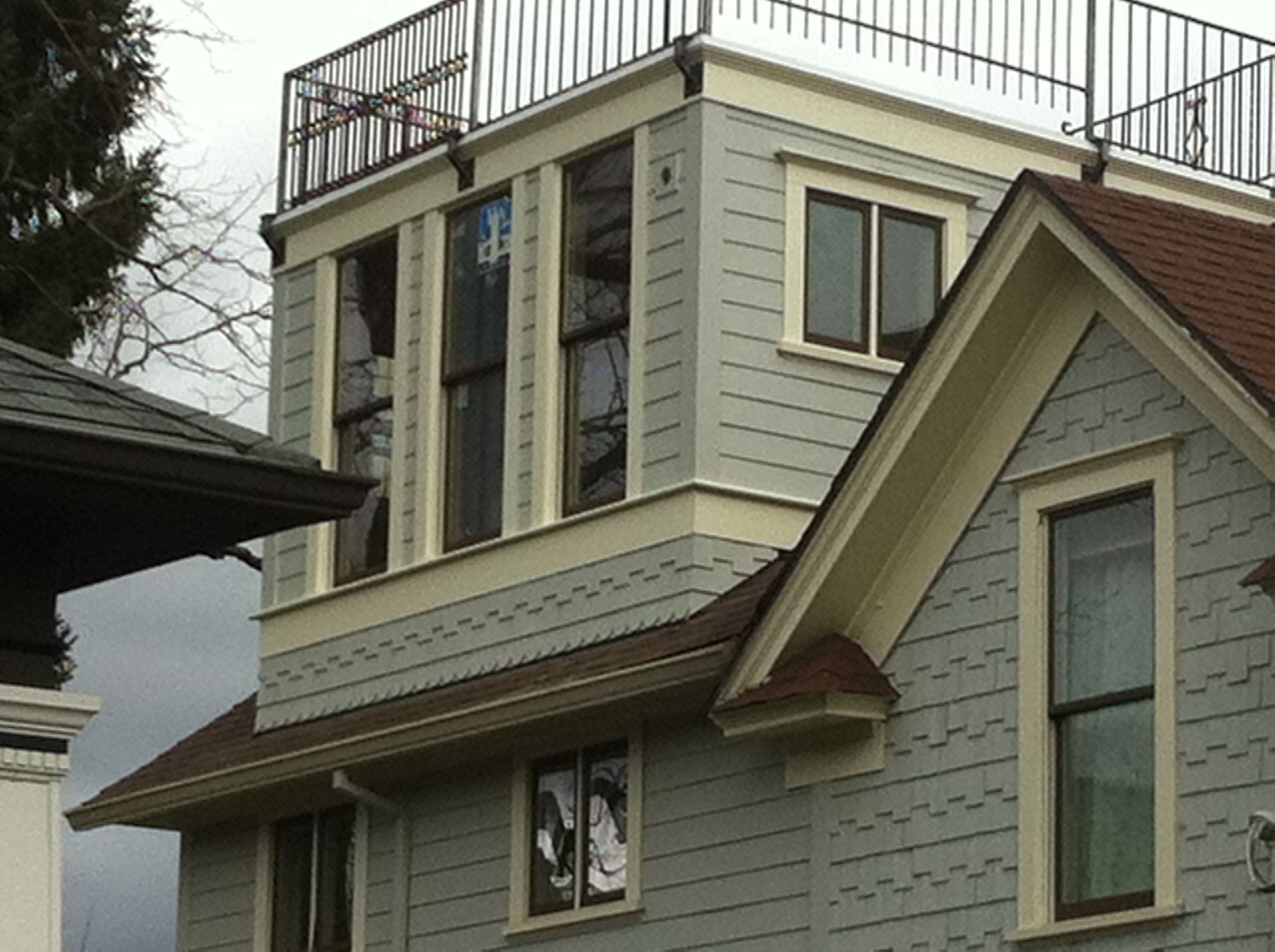 Two-story gray house with cream trim and rooftop deck under overcast sky