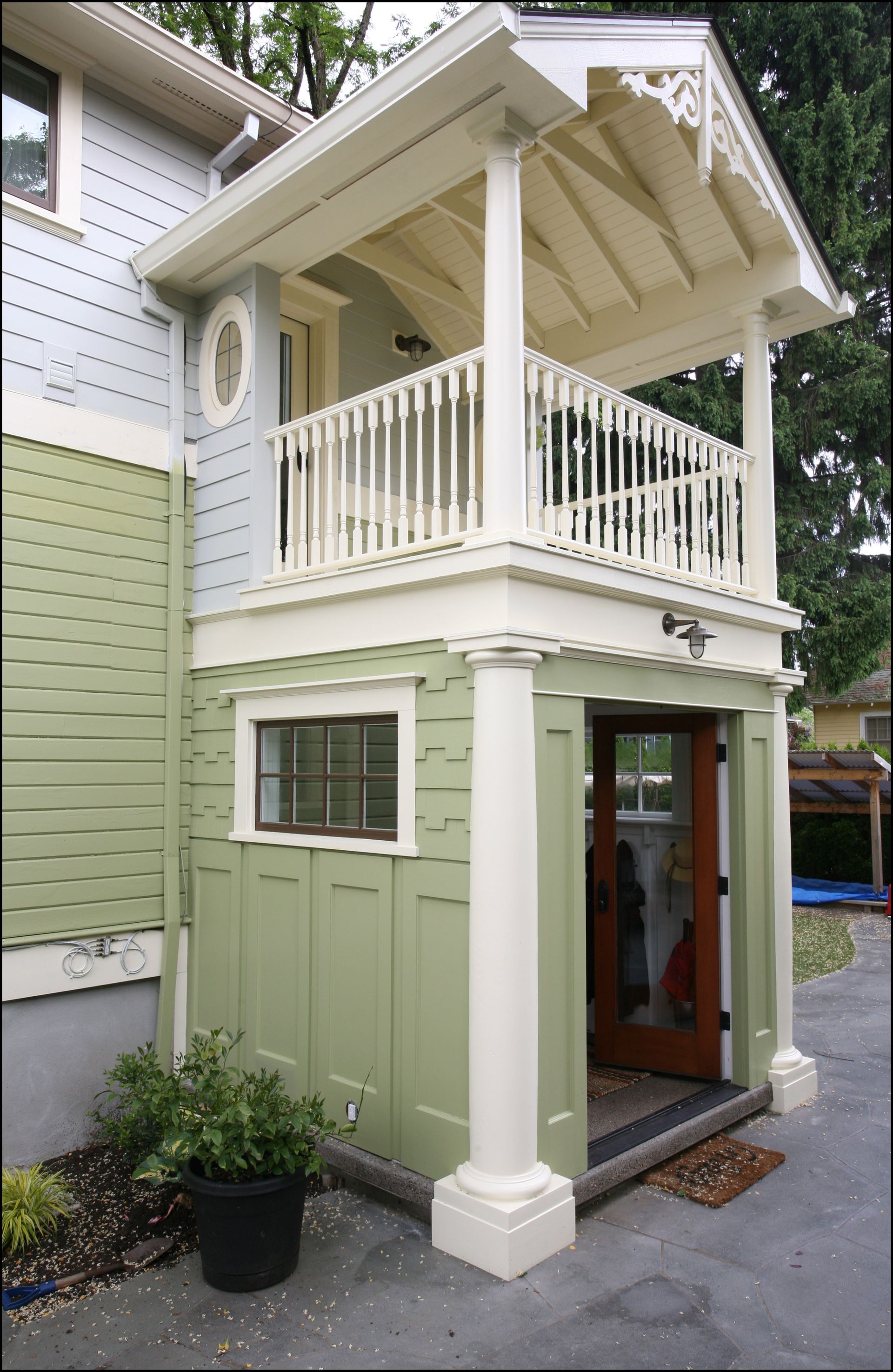Compact two-story green house with white trim and upper balcony entrance on a walkway