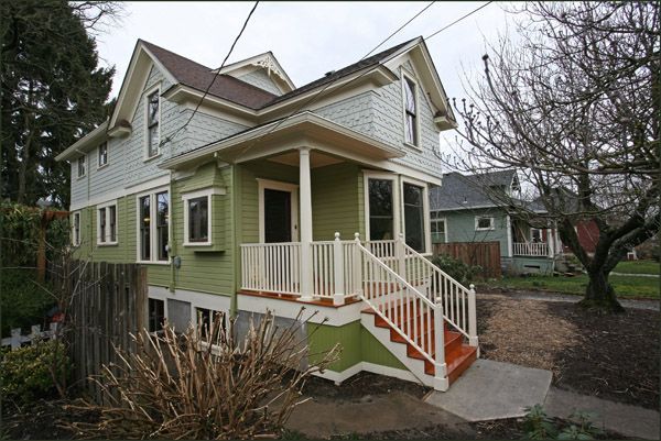 Green two-story house with white trim and a front porch, viewed from the yard on an overcast day