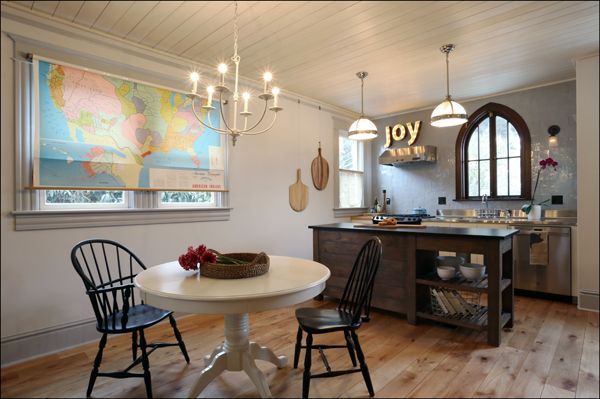 Bright kitchen with round table, black chairs, island, hanging lights, map, and arched window