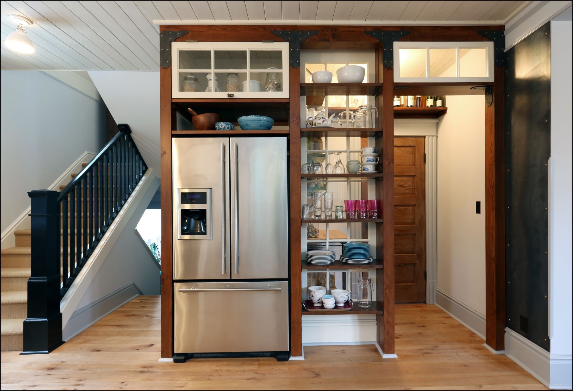 Kitchen with stainless steel fridge, open shelves, and wooden cabinets in a bright hallway area