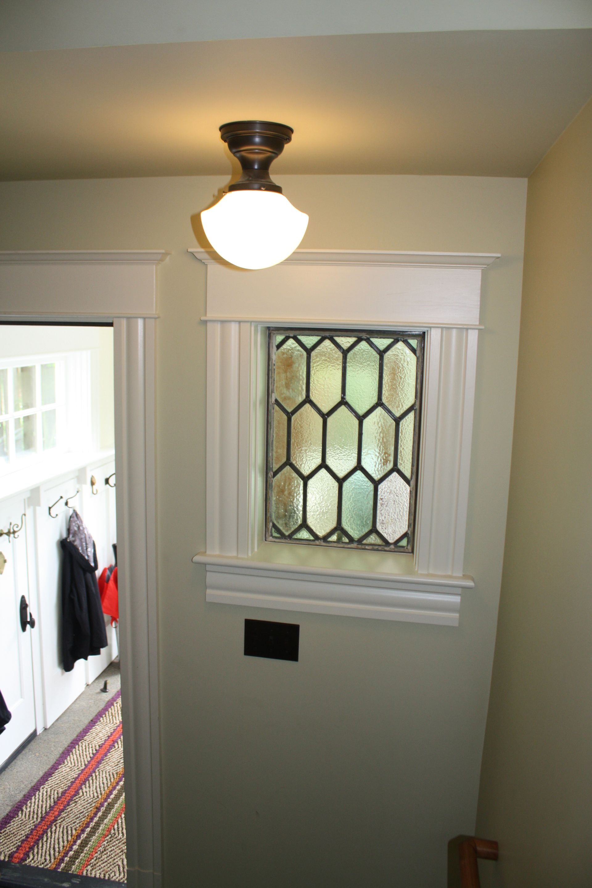 Hallway with ceiling light and small stained-glass window above a wall vent.
