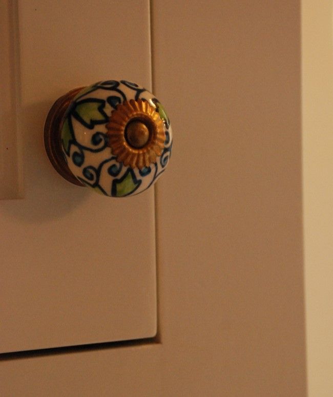 Decorative round ceramic knob with green and blue floral pattern on a beige cabinet door