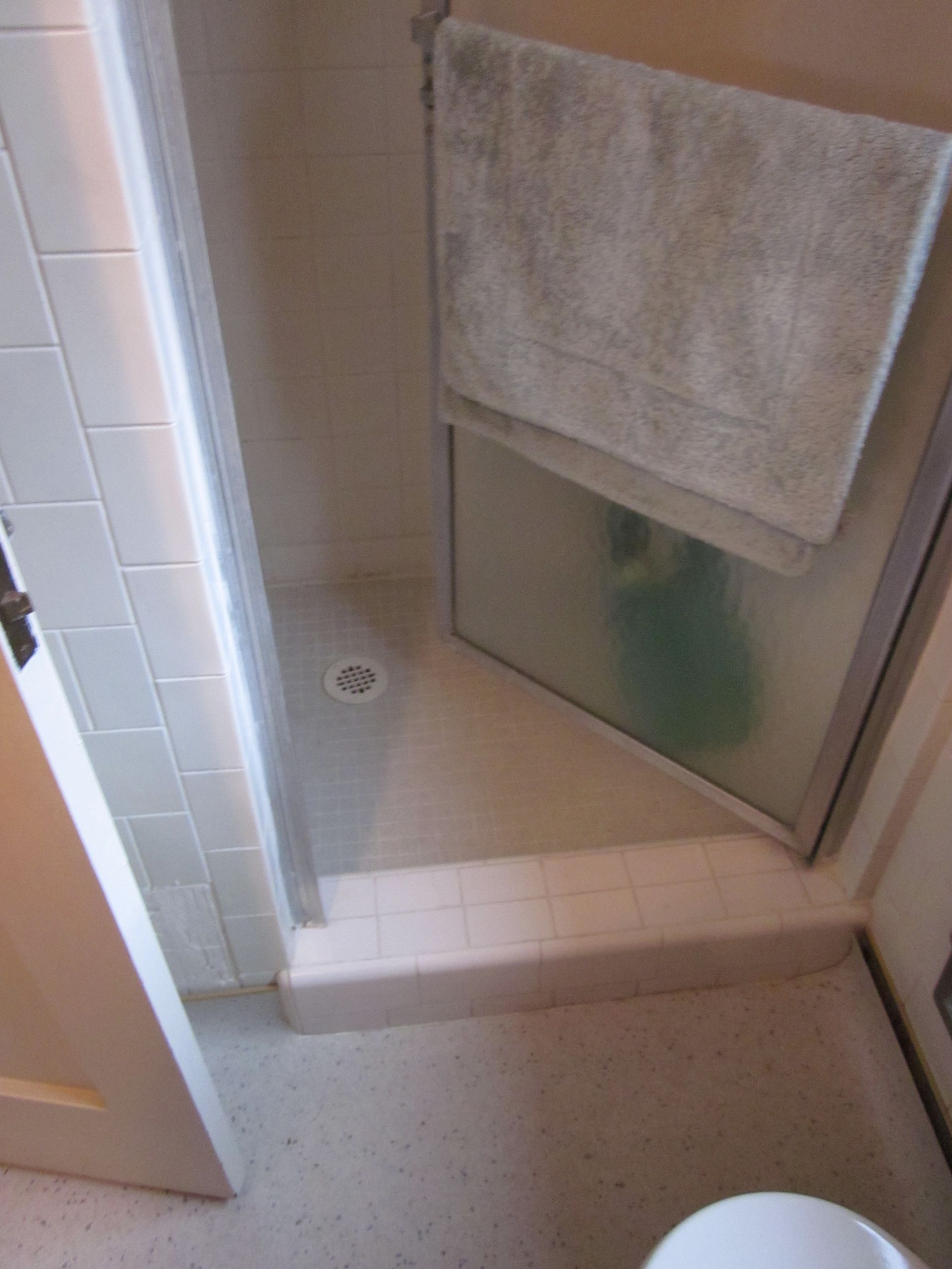 Small bathroom shower stall with tiled floor, frosted glass door, and towel hanging on the door.