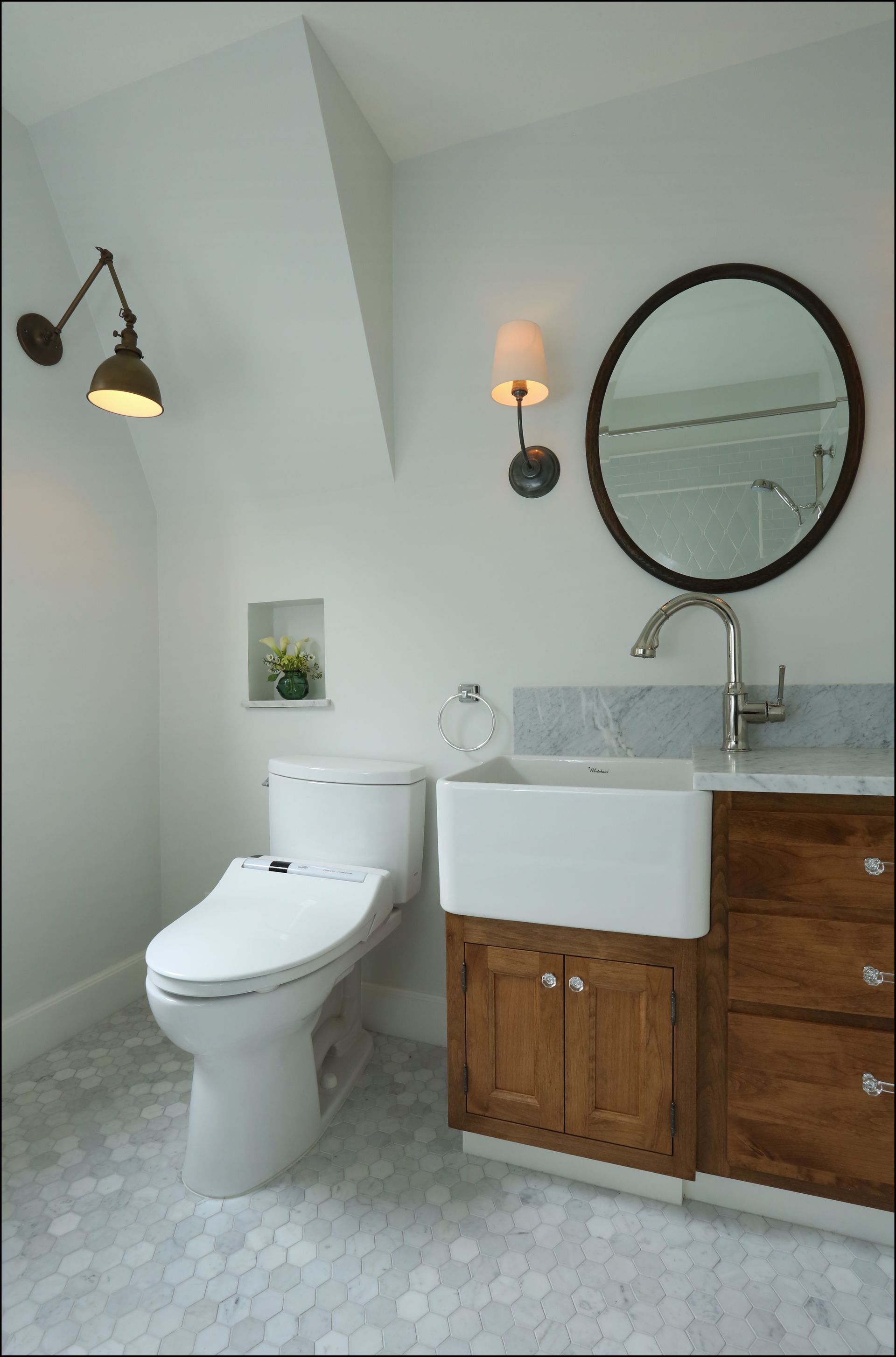 Modern bathroom with white toilet, marble sink, round mirror, wood vanity, and gray hex tile floor