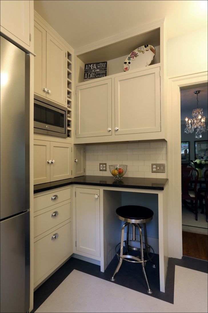 Compact white kitchen with built-in appliances, black countertops, and a stool by a small counter nook.