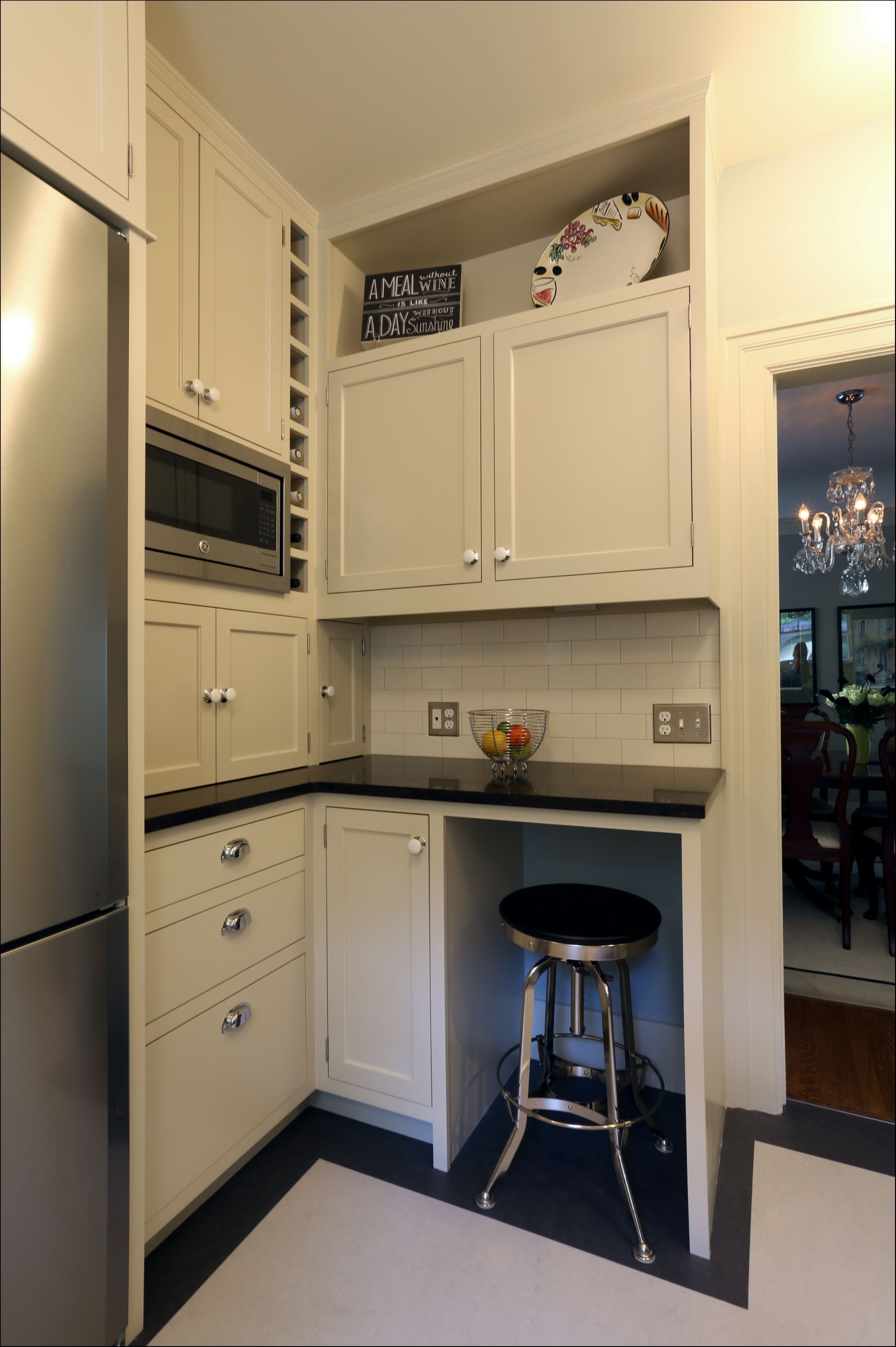 Small white kitchen with cabinets, black countertops, built-in appliances, and a stool by a peninsula.