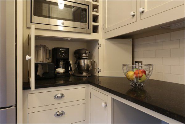 Compact kitchen with microwave, coffee maker, mixer, and bowl of fruit on a dark countertop