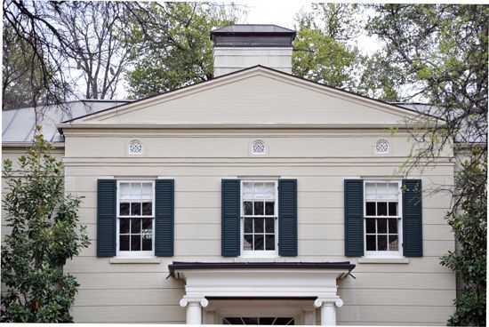 Front of a beige house with dark green shutters and a central dormer window