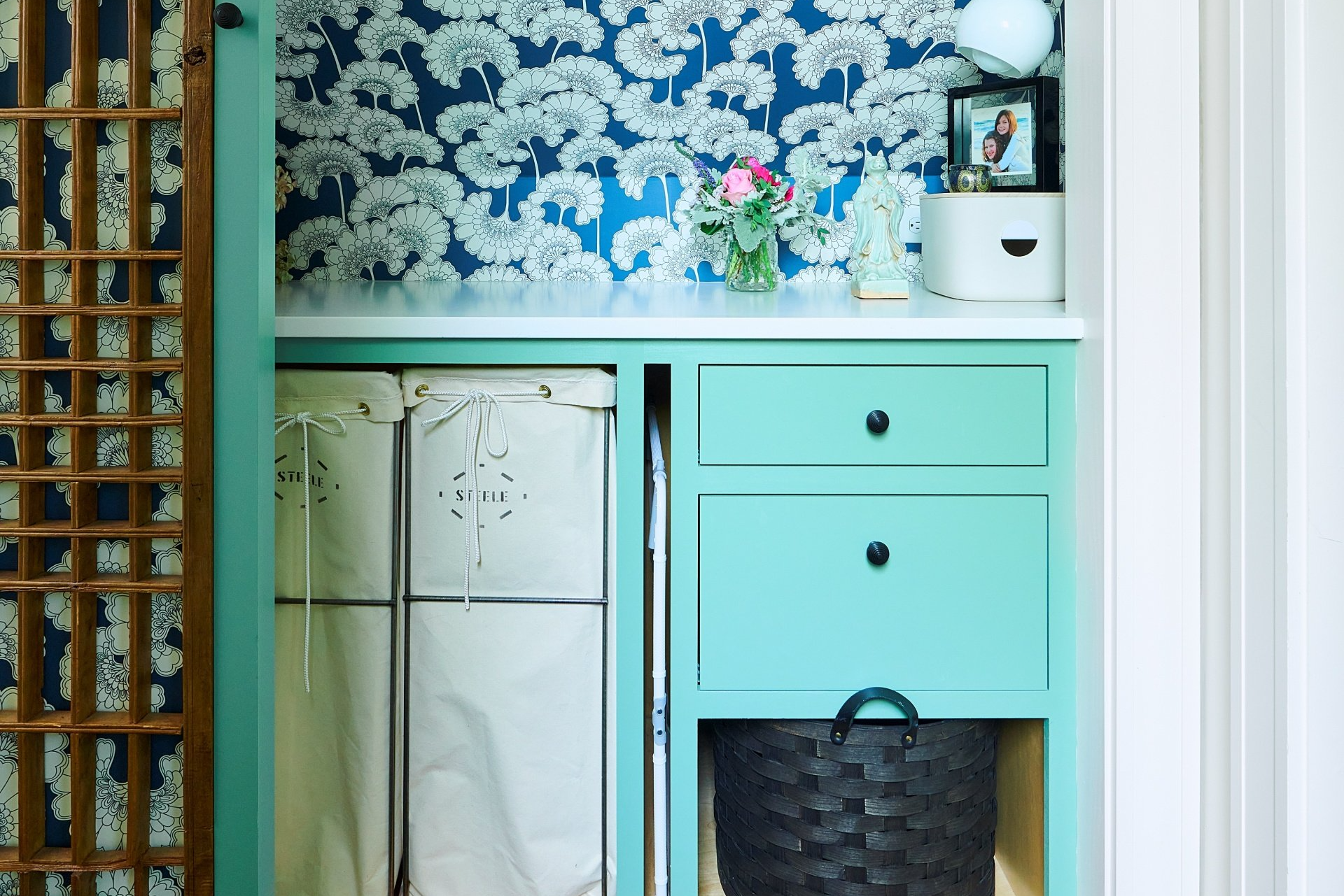 The hallway laundry closet is concealed with a rolling Chinese screen & features cheery wallpaper & built ins.