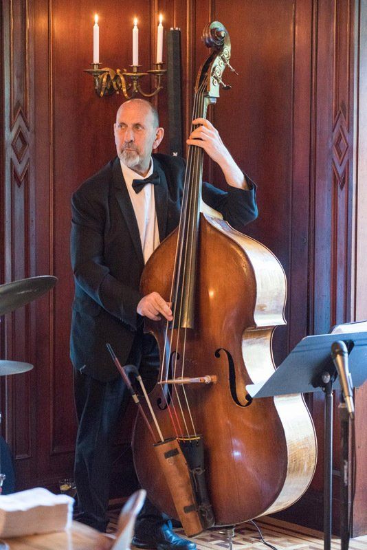 A man in a tuxedo is playing a double bass in front of candles.