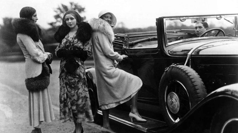 A group of women are standing next to a car in a black and white photo.