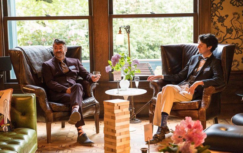 Two men are sitting in chairs in a living room playing jenga.
