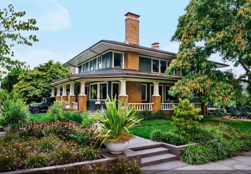 1915 Irvington Prairie-Style Craftsman A large brick house with a large porch is surrounded by trees and bushes.