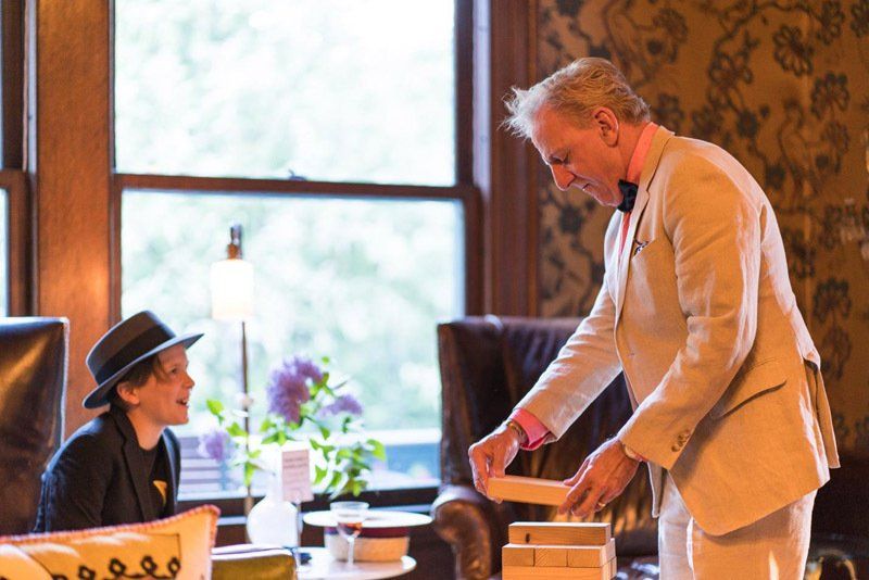 A man in a suit is standing next to a boy in a hat in a living room.