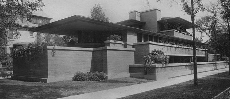 A black and white photo of a large house with a sidewalk in front of it.