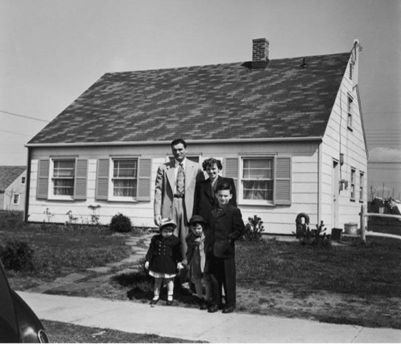 A black and white photo of a family standing in front of a house