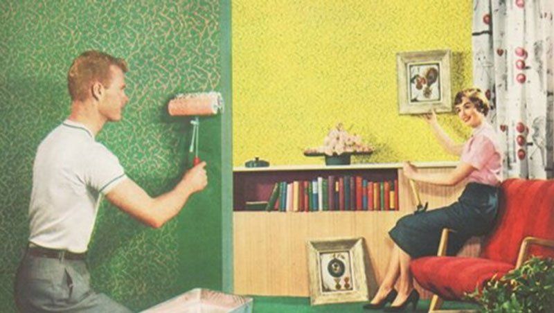 A man is painting a wall while a woman sits in a chair.
