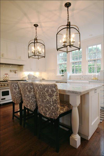 Bright white kitchen with island, patterned bar stools, and hanging pendant lights near large windows