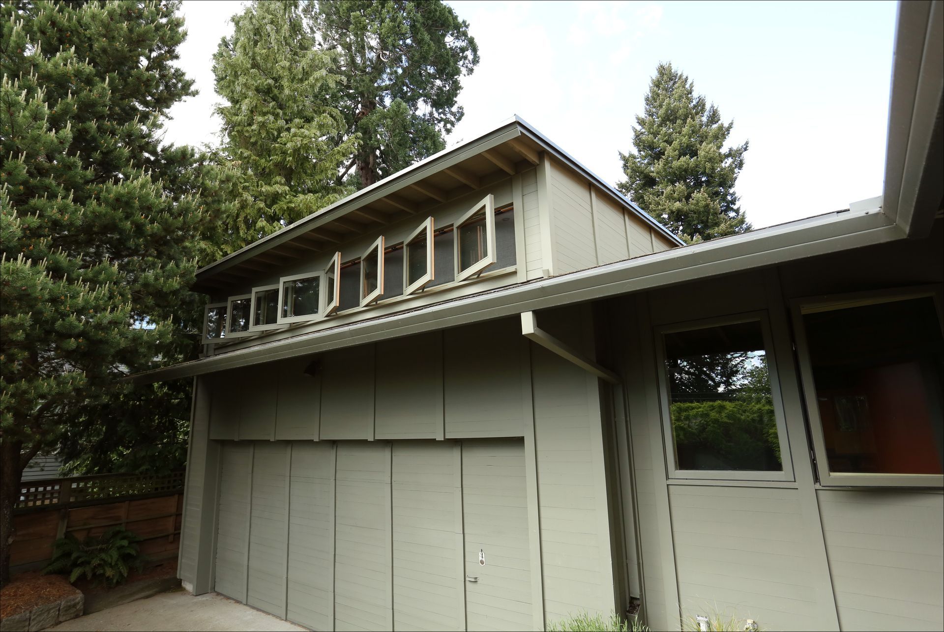 Exterior of a gray house with a sloped roof and upper-row windows, surrounded by trees