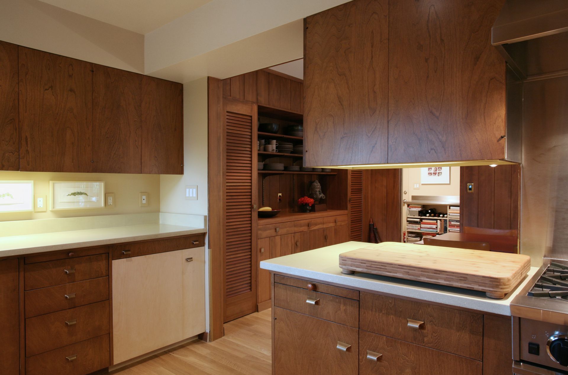 Warm-toned kitchen with wooden cabinets, countertop, and a central island under a large hanging hood.