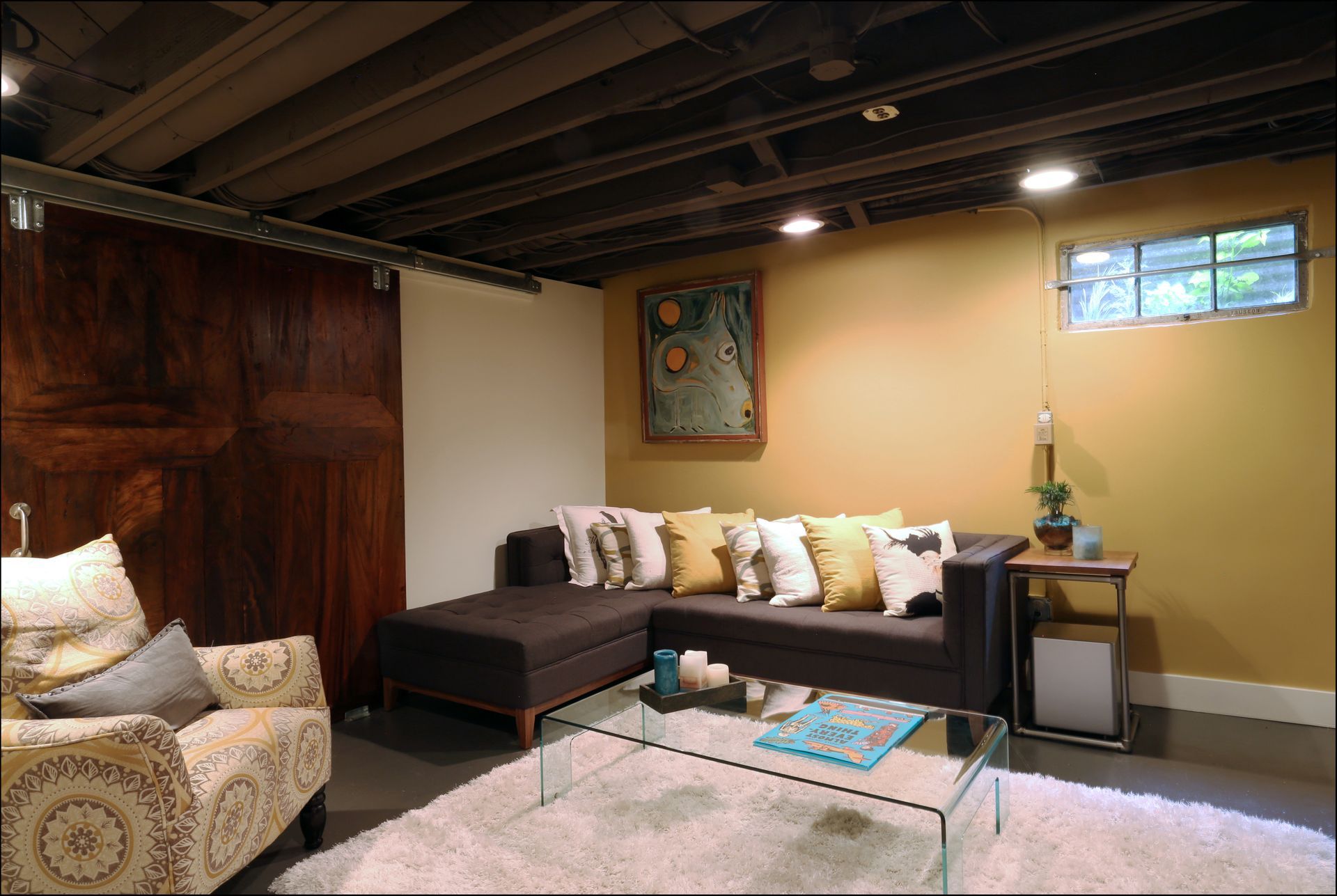 Cozy basement living room with sectional sofa, rug, side table, and exposed ceiling beams