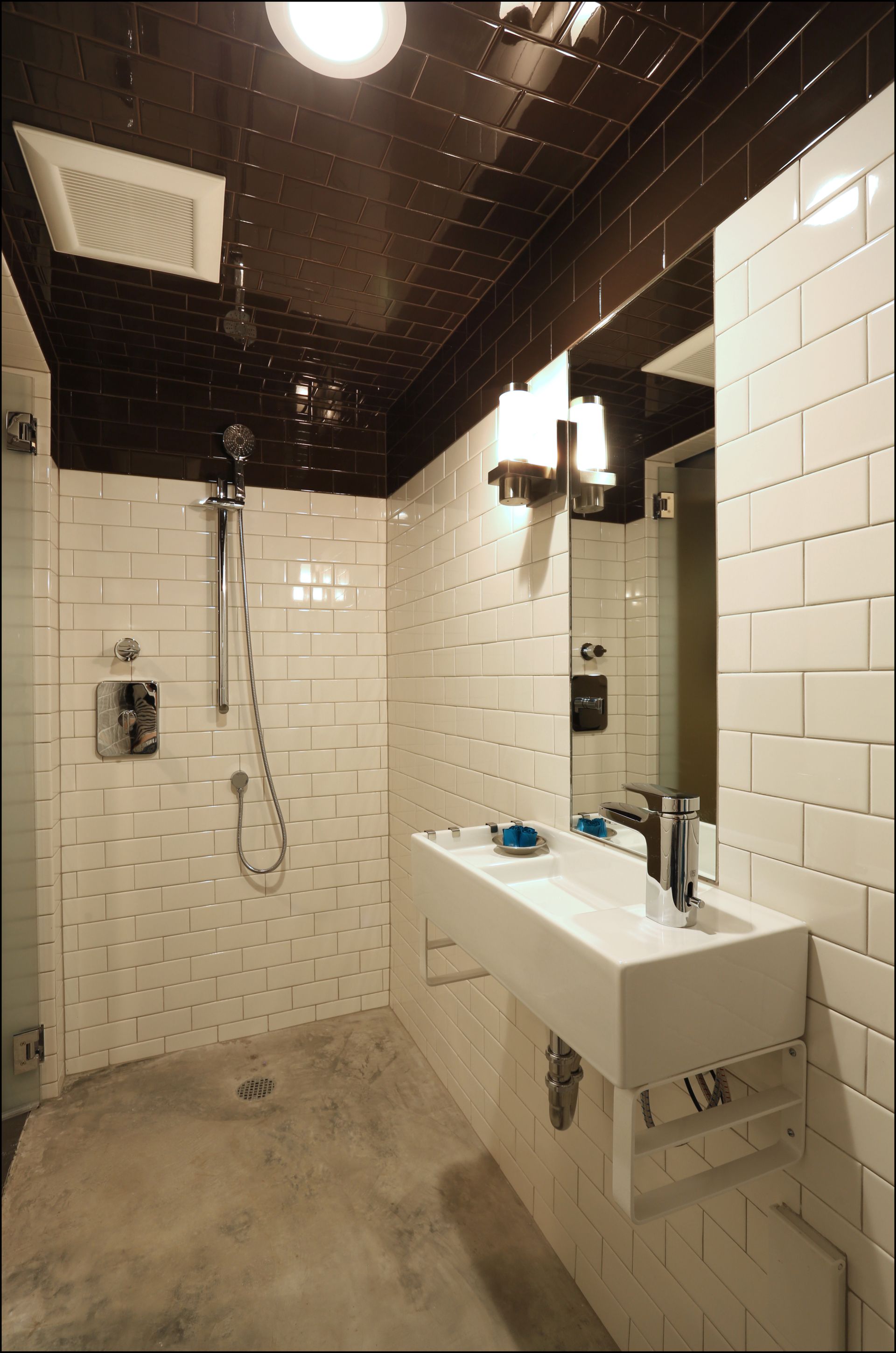 Small tiled bathroom with shower, white sink, mirror, and dark ceiling.