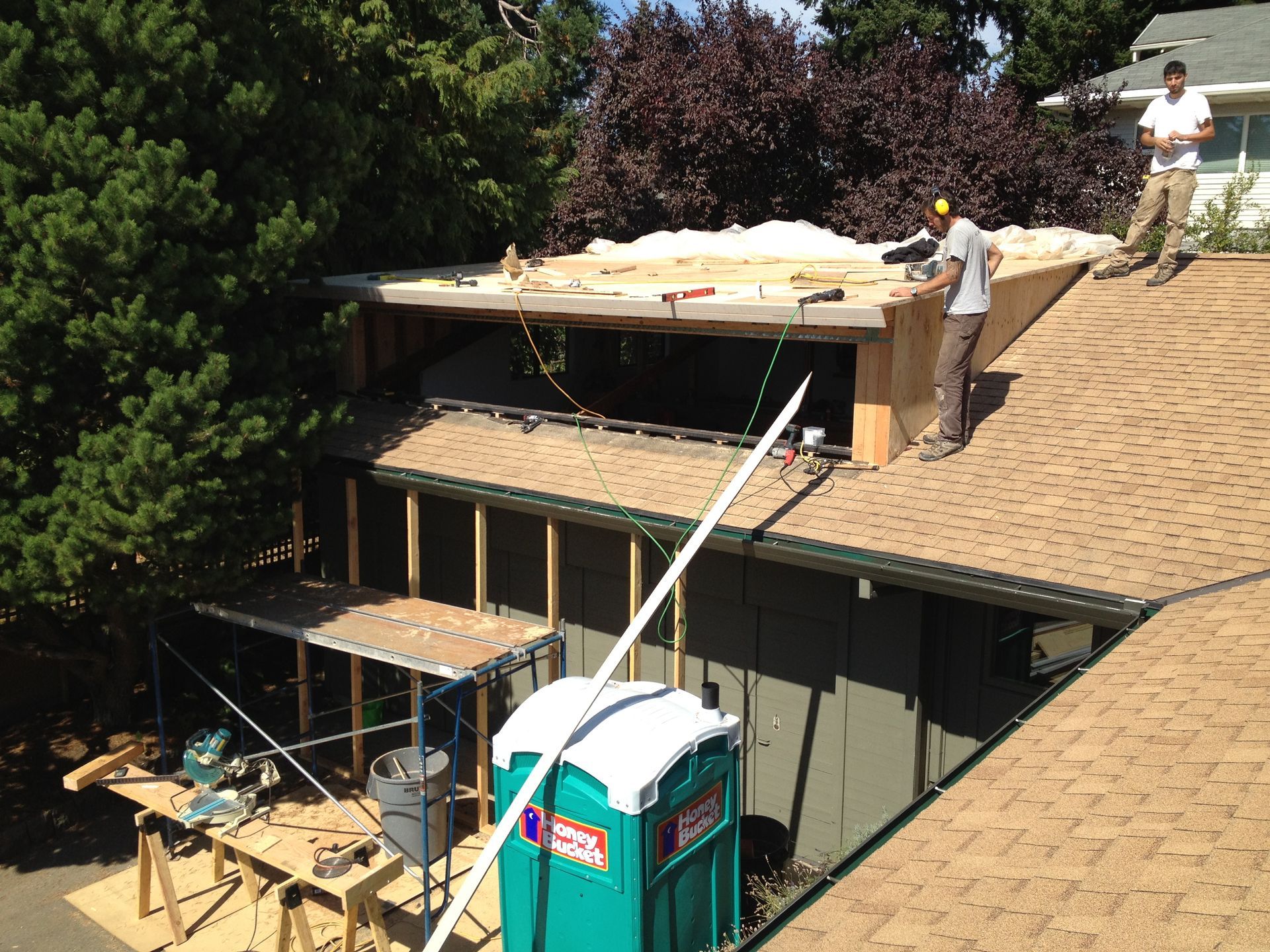 Workers on a roof installing a large panel, with a crane lifting materials beside the house.