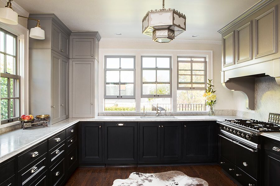 Bright modern kitchen with black lower cabinets, gray uppers, marble counters, and large windows