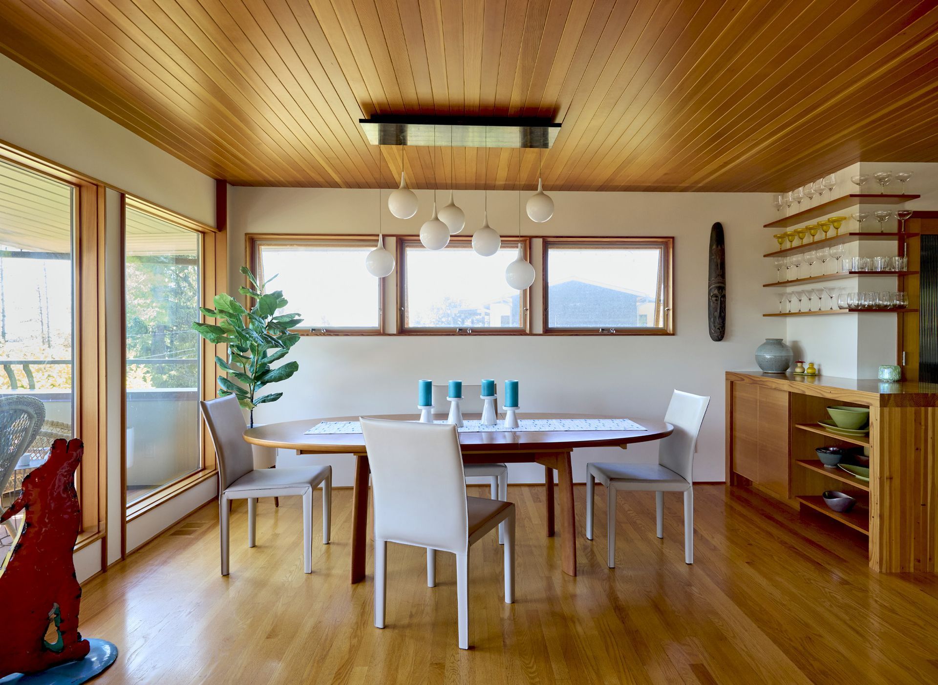 The living room shares walls with the dining room on the upper level. Under a tongue-and-groove vertical-grain fir ceiling is the sleek dining table with a trio of clerestory windows and a custom light fixture above.