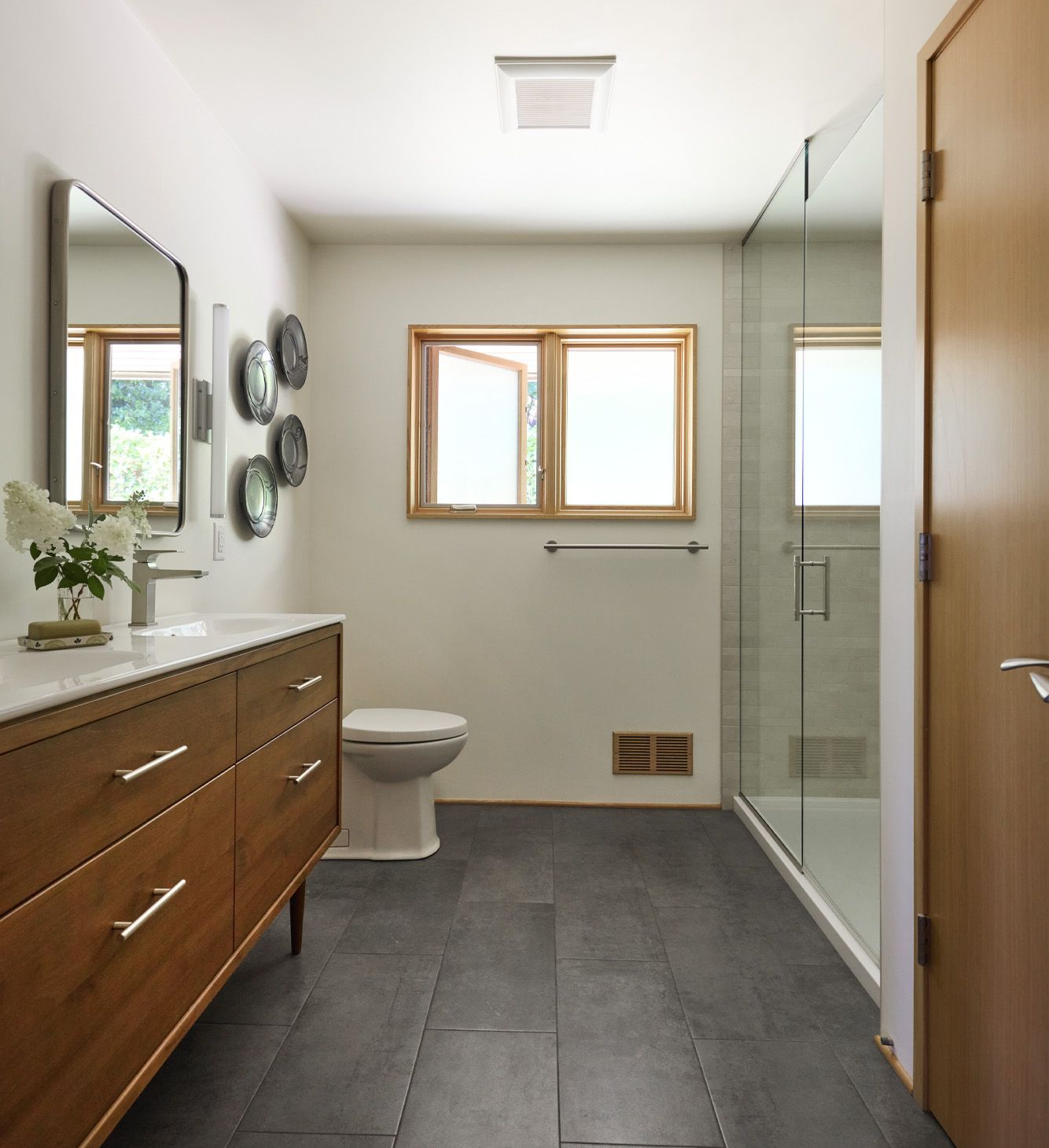 The generous guest bath is fresh and welcoming with creamy white walls, a teak vanity, graphite floor tile and plenty of morning light from the East - facing window.