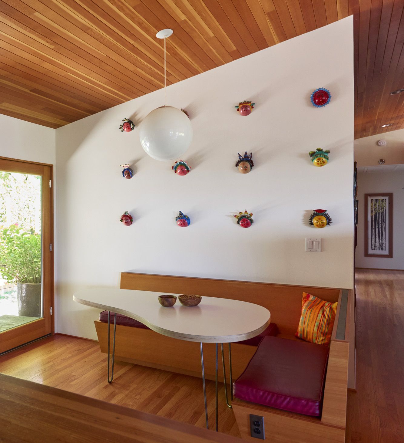 The cool kitchen banquette features book storage, electrical outlets, and a kidney-shaped tabletop made to fit the space perfectly, under a collection of Mexican folk art masks.